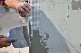 Contractor repairing stucco wall with mesh reinforcement and trowel in Reno, NV.